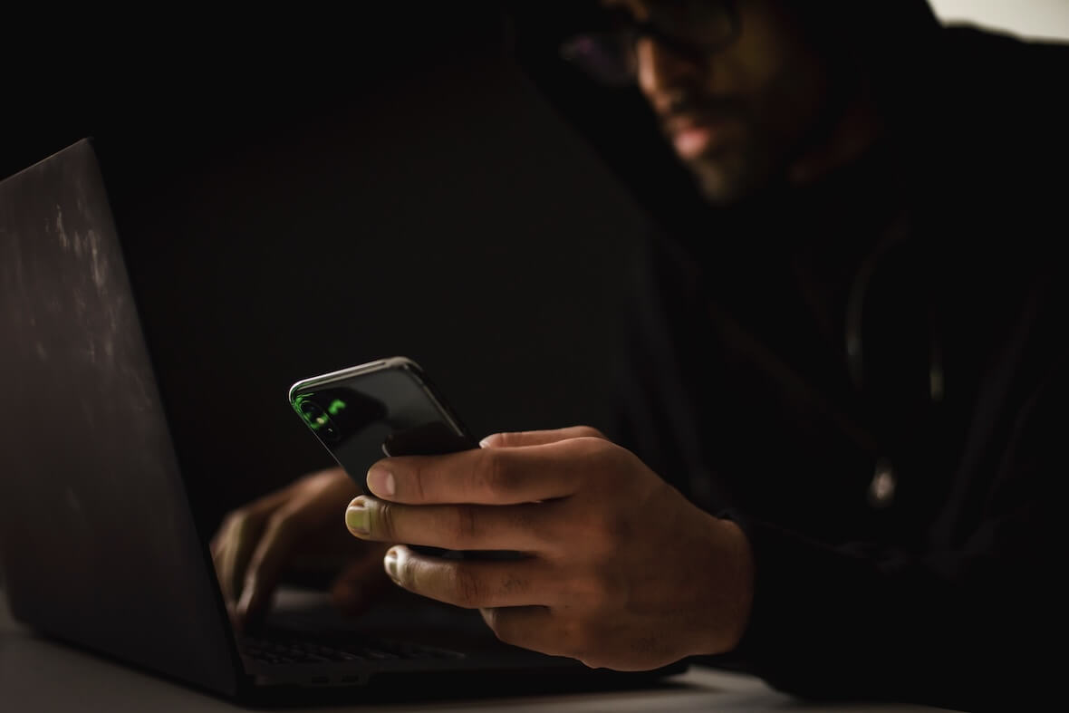 An image of a hacker using a laptop and a cell phone.