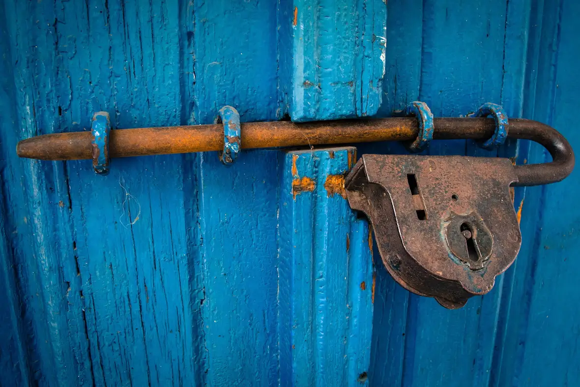 An image of a padlock and bolt on a blue barn door.